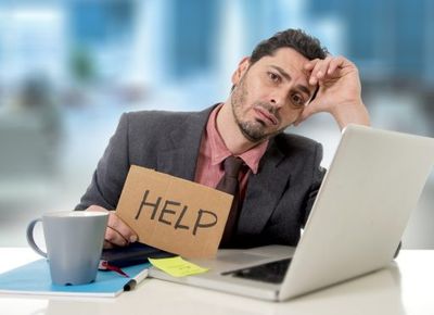 young businessman at office desk working on computer laptop asking for help holding cardboard sign looking desperate and depressed in business stress overwhelmed and overwork concept