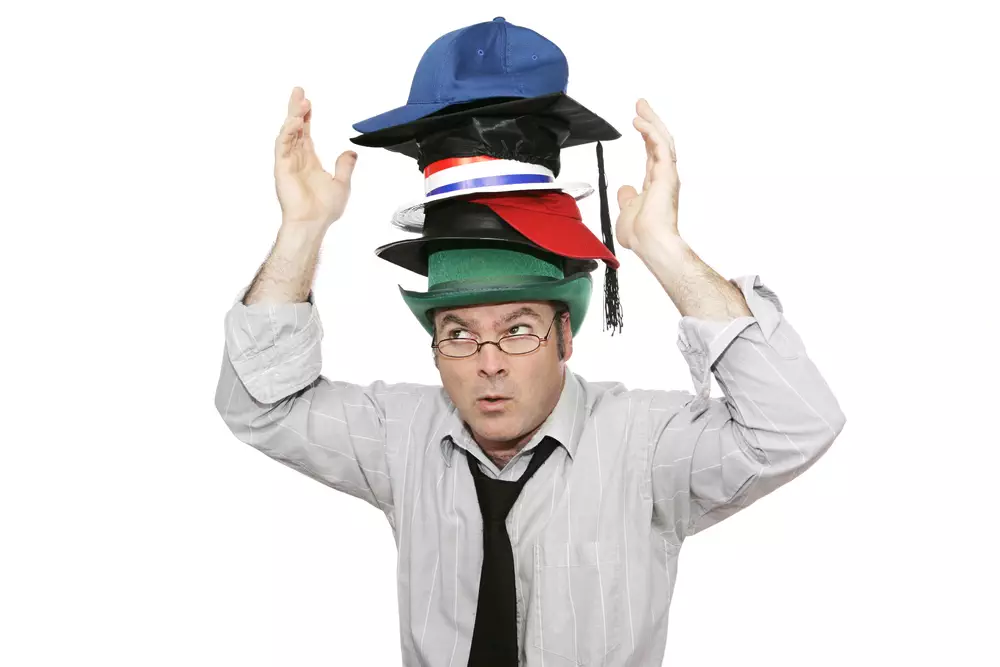 A businessman overwhelmed by too much responsibility - wearing too many hats. Isolated on white.