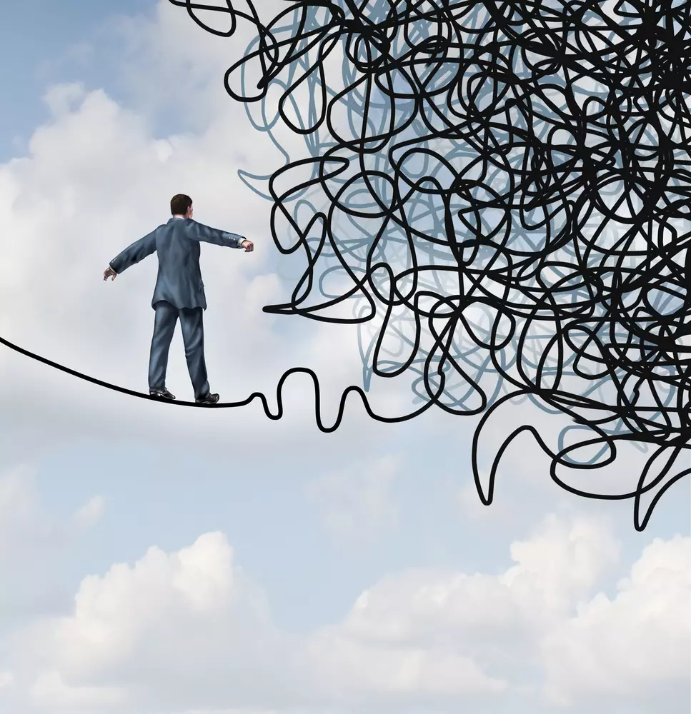 Risk confusion business concept with a businessman on a high wire tight rope walking towards a tangled mess as a metaphor and symbol of overcoming adversity in strategy and finding solutions through skilled leadership facing difficult obstacles.