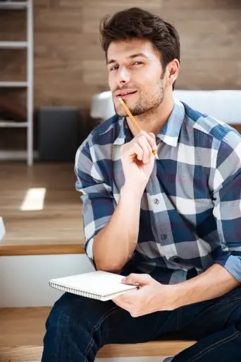 Thoughtful young man with notepad sitting and thinking at home