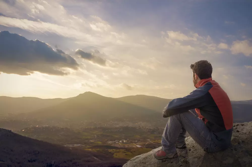 Man on top of mountain sitting on the rock watching a nice sunrise in the village