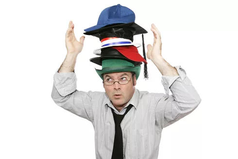 A businessman overwhelmed by too much responsibility - wearing too many hats. Isolated on white.